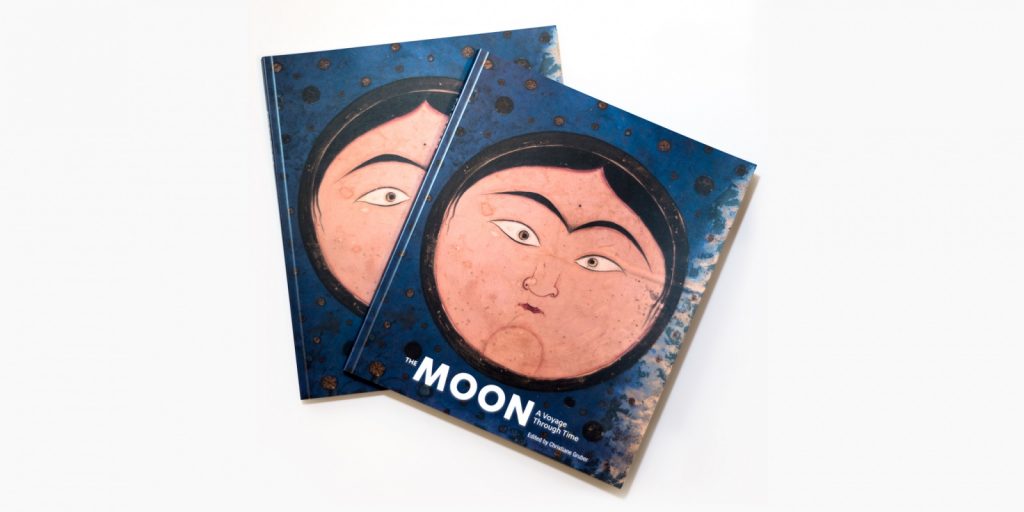 Two books lay stacked on top of one another, both featuring a round face on a blue background. White text reading The Moon: A Voyage Through Time is printed at the bottom.